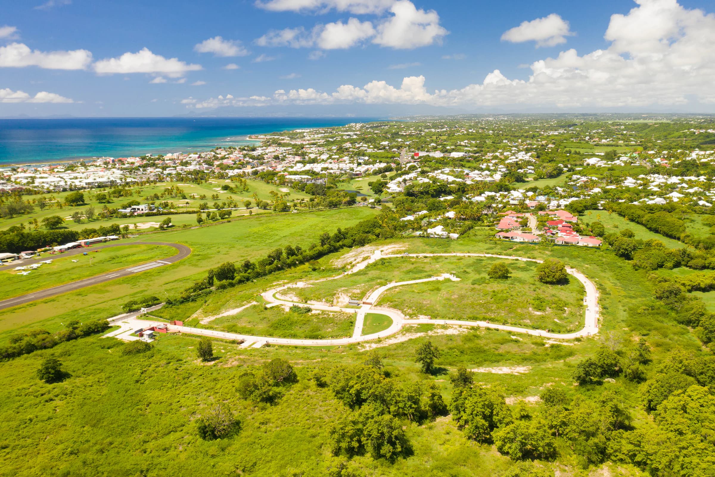 Vue aérienne du lotissement Belles Rives à Anse Champagne en phase de viabilisation, avec en arrière-plan l'aérodrome de Saint-François, le golf international, le bourg, la marina, le lagon et la silhouette de Basse-Terre à l'horizon